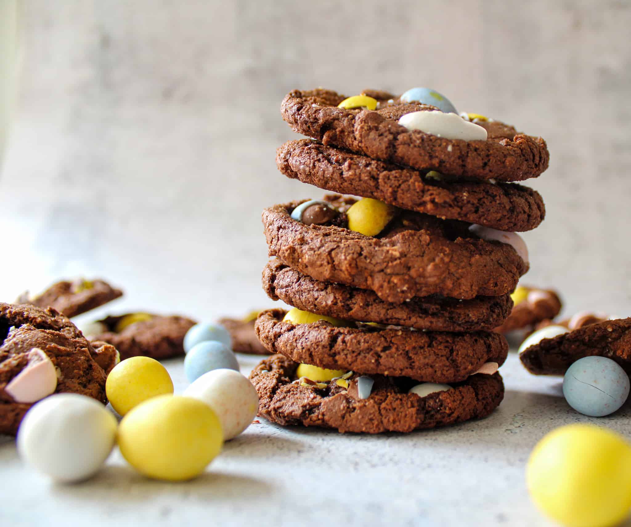 A stack of Cadbury egg brownie cookies with Cadbury eggs scattered around. 