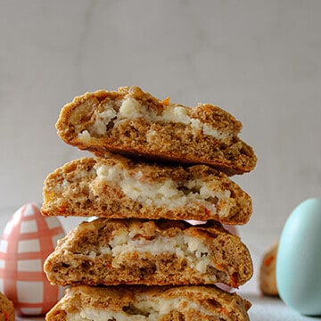 Stuffed carrot cake cookies stacked on top of each other with Easter eggs in the background.