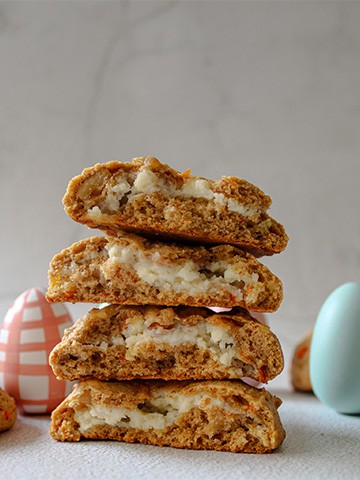 Stuffed carrot cake cookies stacked on top of each other with Easter eggs in the background.