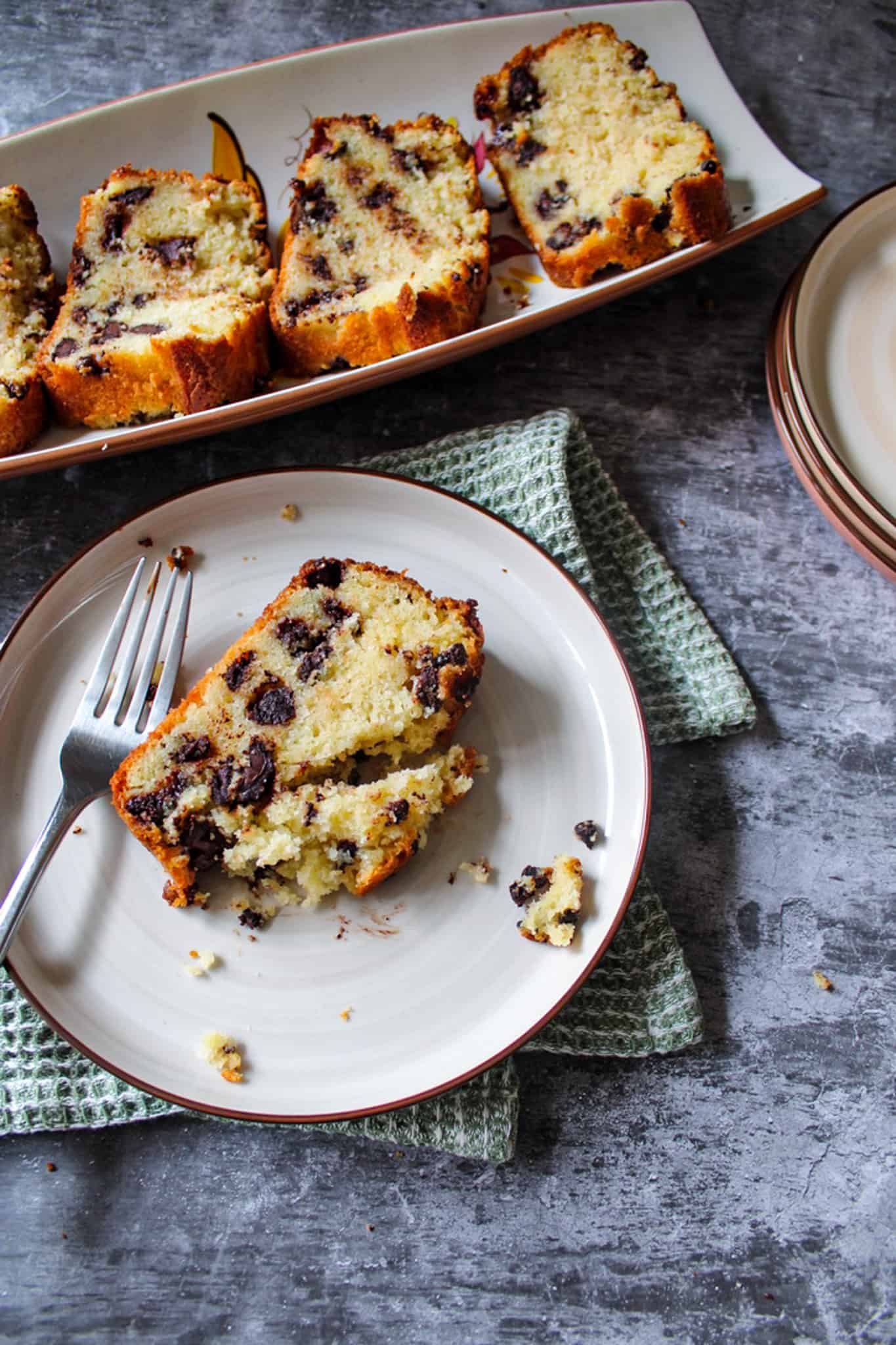 A piece of chocolate chip loaf cake with slices in the back. 