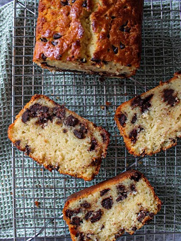 Slices of chocolate chip loaf cake and the rest of the loaf cake on a cooling rack.