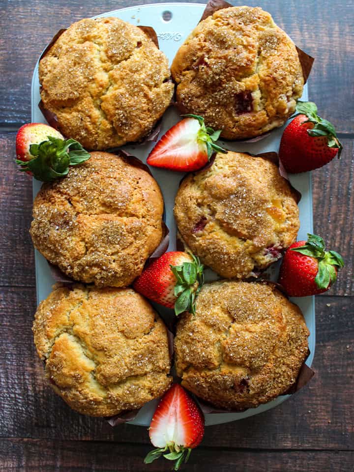 Strawberry cheesecake muffins in a jumbo muffin tin with strawberries scattered around.