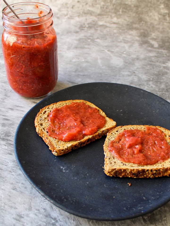 Strawberry rhubarb jam on toast on a plate with the jam in a jar in the background