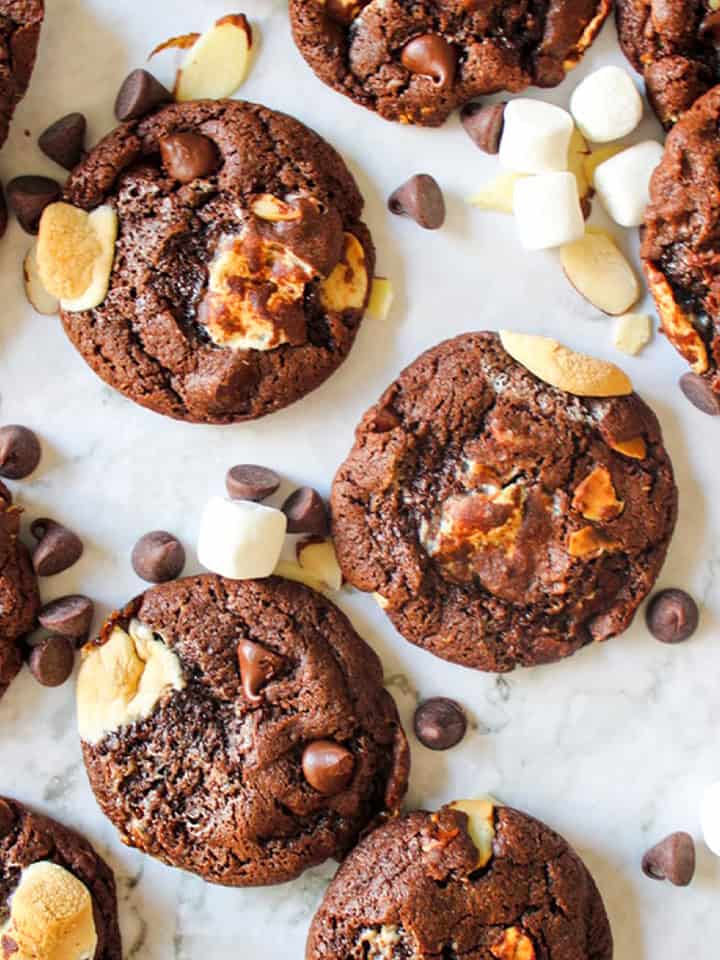 Rocky road cookies on a table with rocky road toppings scattered around.