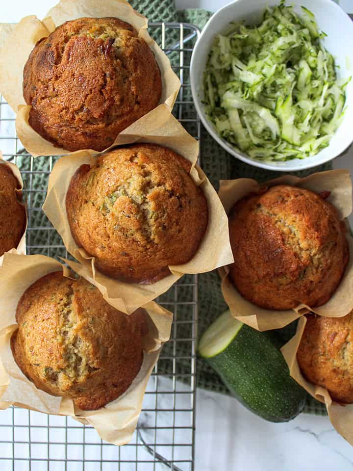 Buckwheat muffins on a rolling rack with shredded zucchini in a bowl.