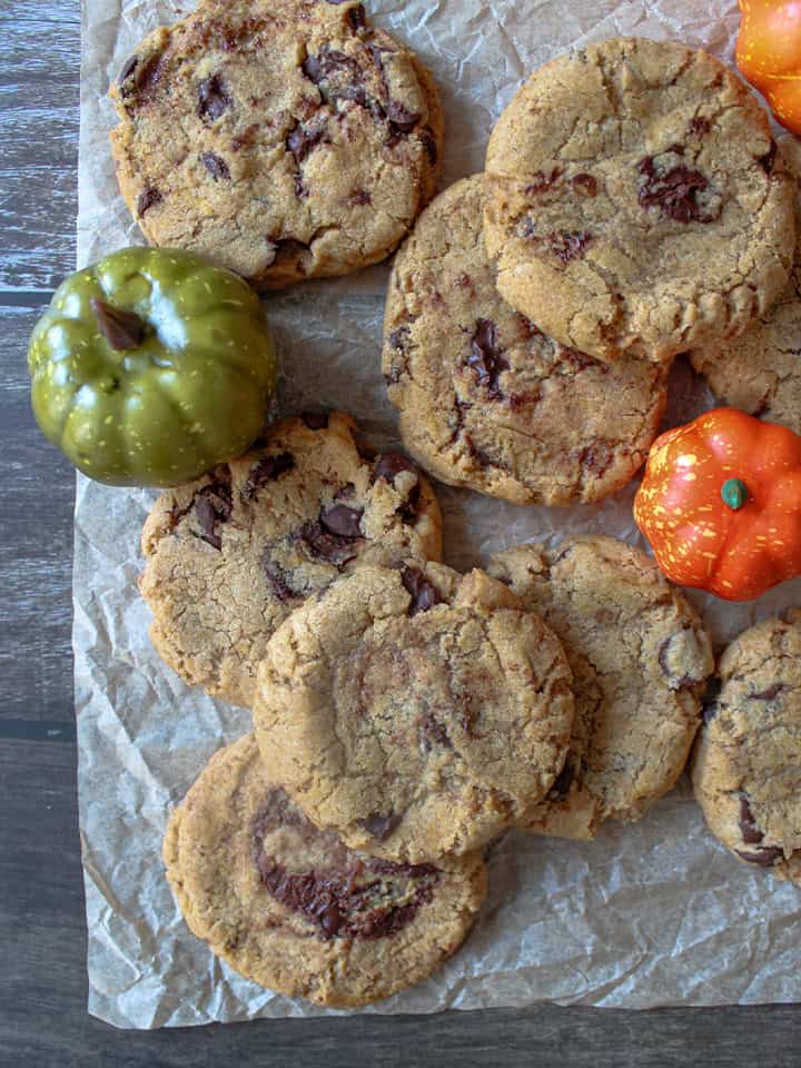 Pumpkin chocolate chip cookies on a piece of parchment paper with ornamental pumpkins.