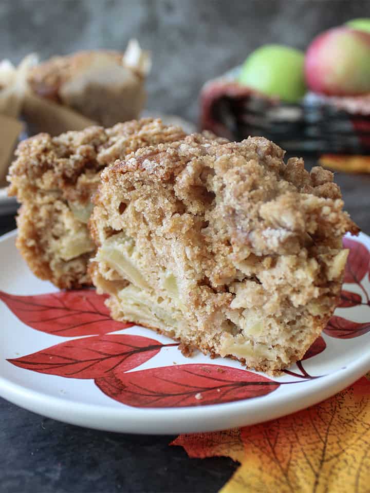 Apple crumble muffin split open on a white plate with red leaves.