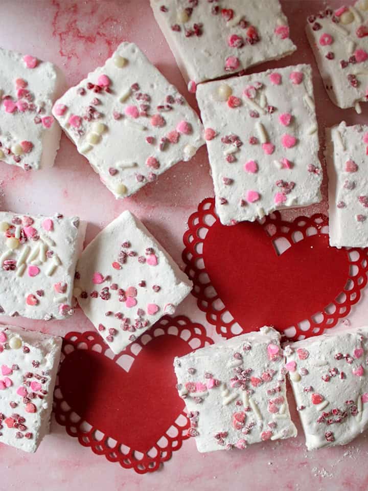 Valentine's Day Marshmallow scattered around on top of decorative Valentine's Day hearts.