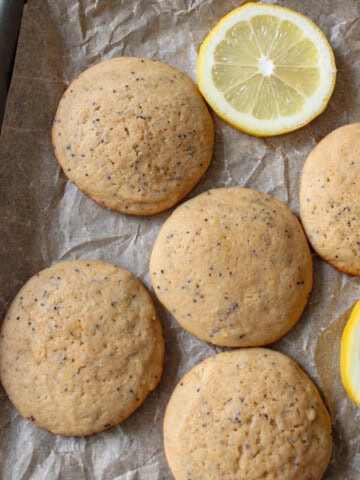 Lemon poppy seed muffin top cookies on a cookie sheet with slices of lemon.